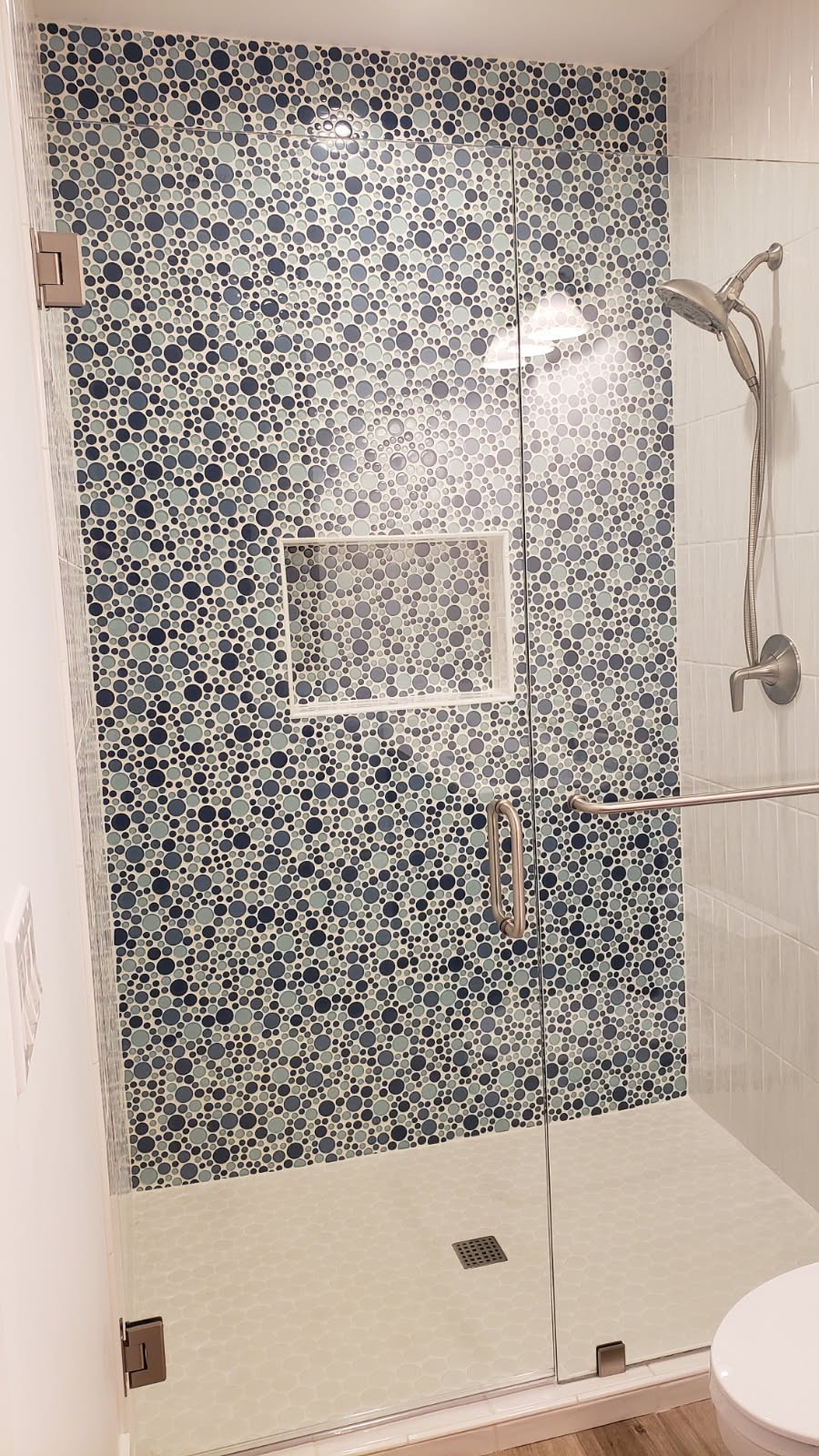 Custom tile shower with blue pebble mosaic accent wall and glass door in Wenatchee WA